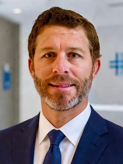Portrait of a man in a suit and tie with a beard, smiling.