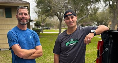 Two men casually posing outdoors near a vehicle on a cloudy day.