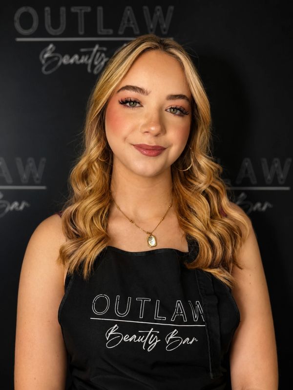 Young woman with styled blonde hair wearing a black Outlaw Beauty Bar apron.