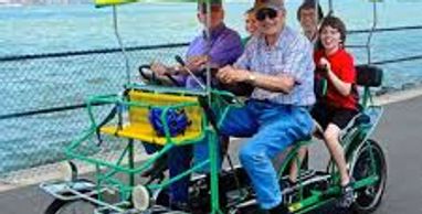 Four people riding a yellow-canopied pedal bike by the water.