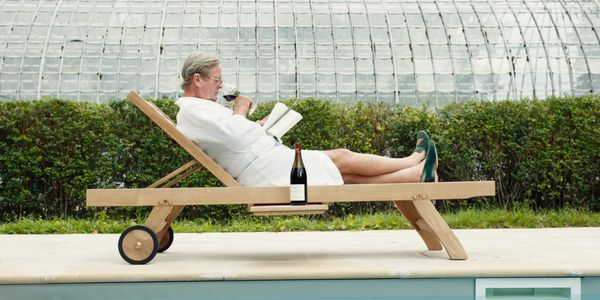 Person relaxing by the pool with a book and wine.