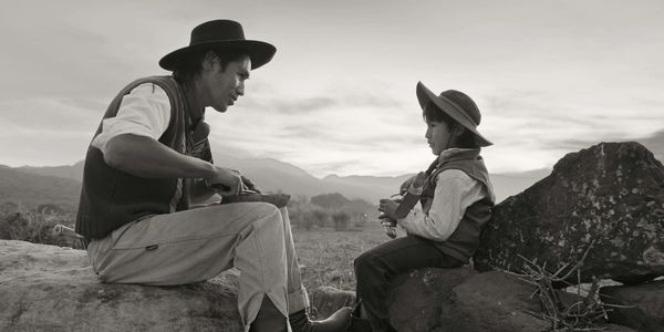 Two cowboys sitting on rocks having a moment.