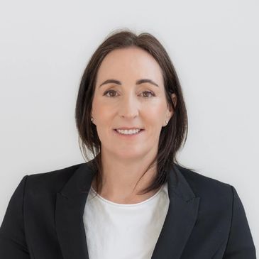 Professional woman smiling in a black blazer and white top against a plain background.