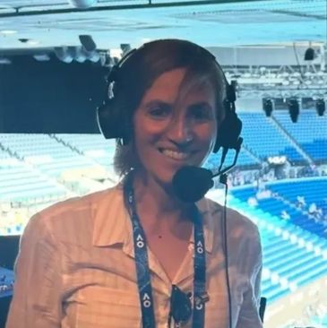 A woman wearing a headset and lanyard at a sports stadium.
