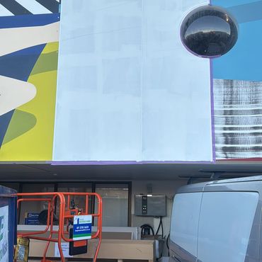 A blank billboard above a building's entry with a van and equipment below.