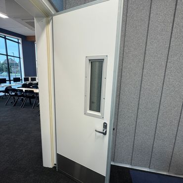 Partially open white door with window in a modern office.