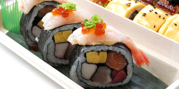 A tray of assorted sushi rolls with toppings and a drink in the background.