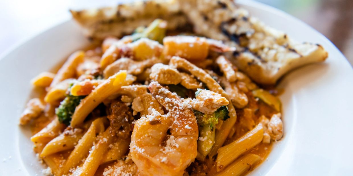 a white plate topped with pasta covered in sauce topped with some meat