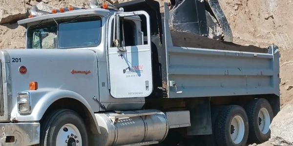 Dump truck being loaded with dirt by an excavator at a construction site.