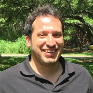 Rabbi Baruch, with dark brown hair and wearing a black polo shirt, is smiling at the camera.