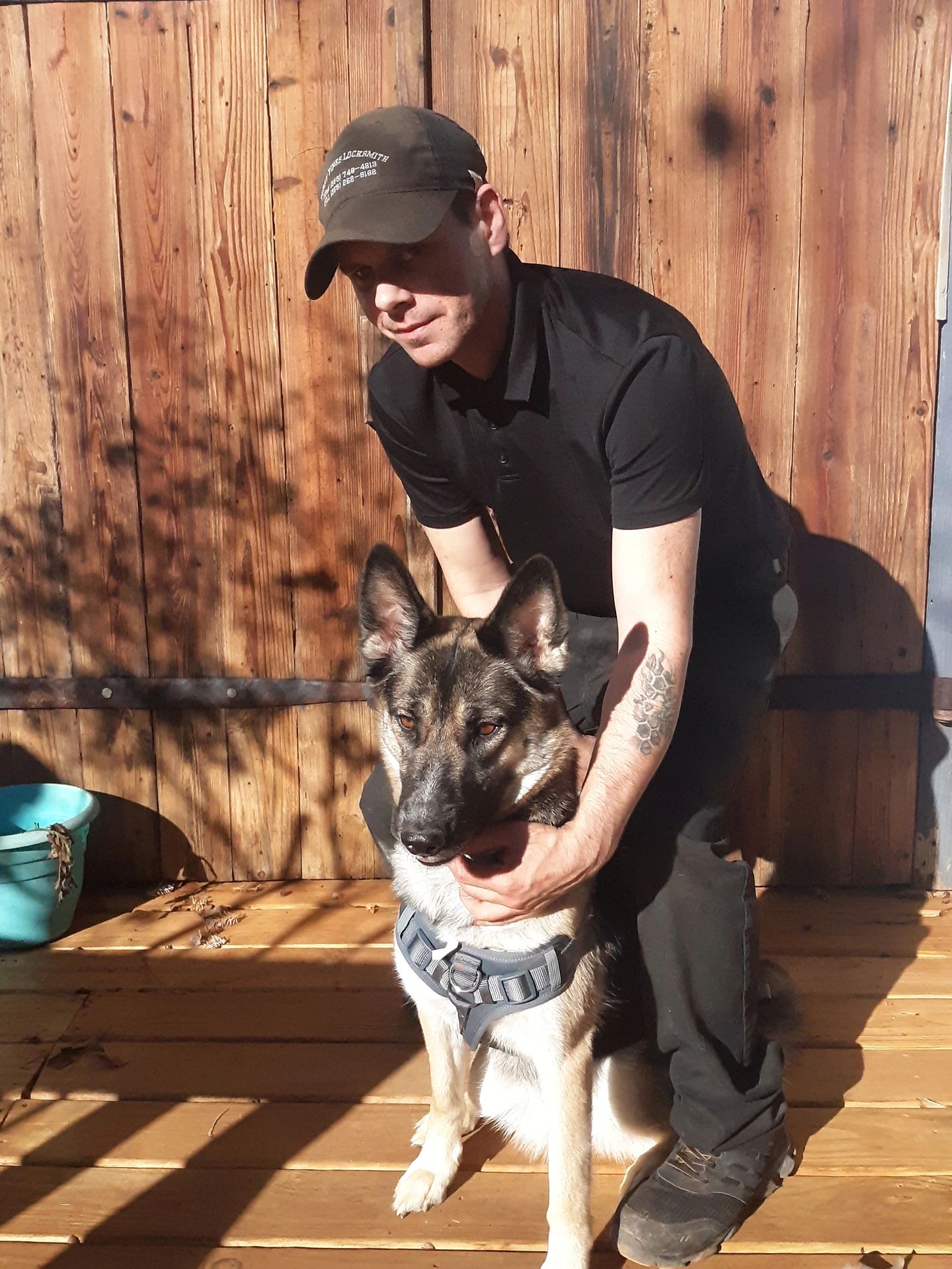 Man in black shirt and cap with a German Shepherd dog on a wooden deck.