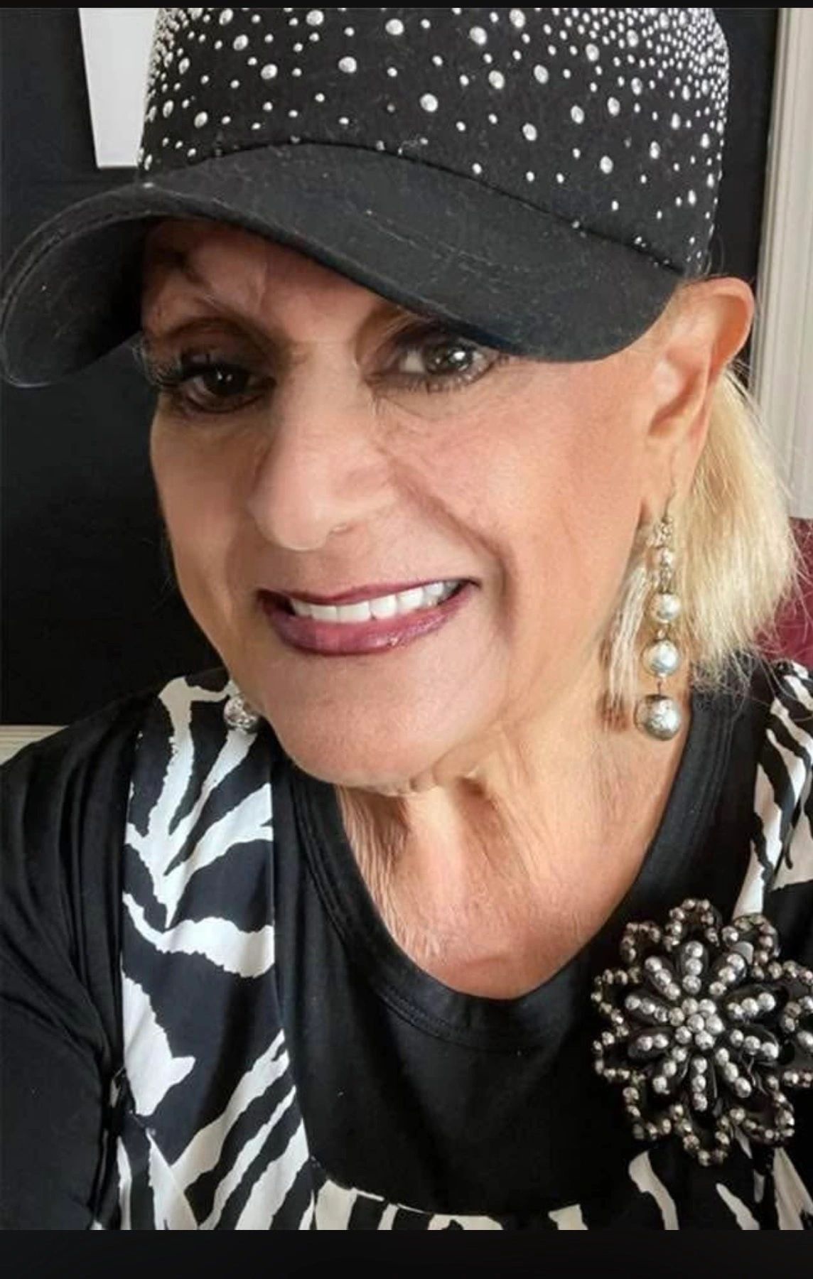 Smiling woman wearing a black cap with rhinestones and zebra print clothing.