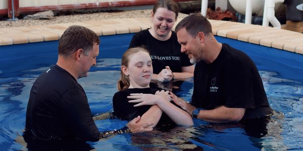 A girl being baptized in a pool by two men and a woman.