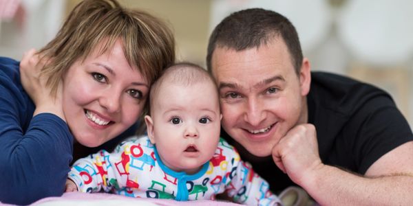 Smiling parents with their baby lying down together.