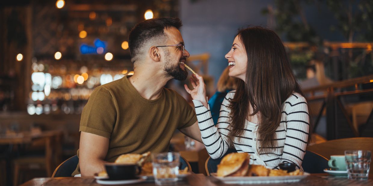 Couple sharing food and laughing at a cozy restaurant.