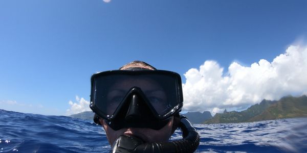Person wearing snorkeling gear in the ocean with mountains in the background.