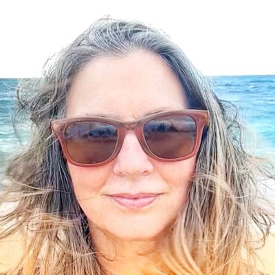 Woman with sunglasses smiling near the ocean on a sunny day.