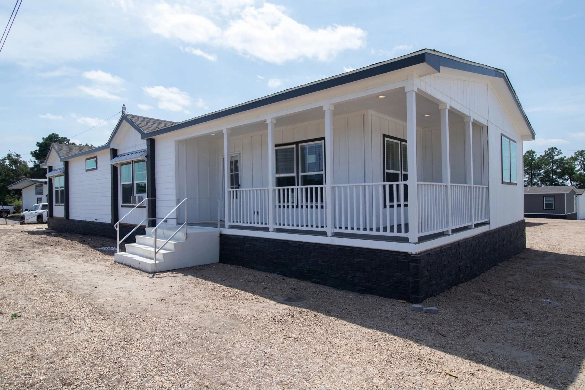White modern manufactured home with a spacious front porch and steps.