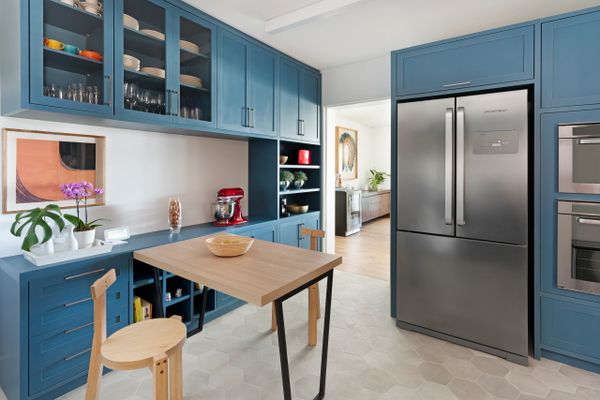 Modern kitchen with blue cabinets, wooden table, and stainless steel refrigerator.