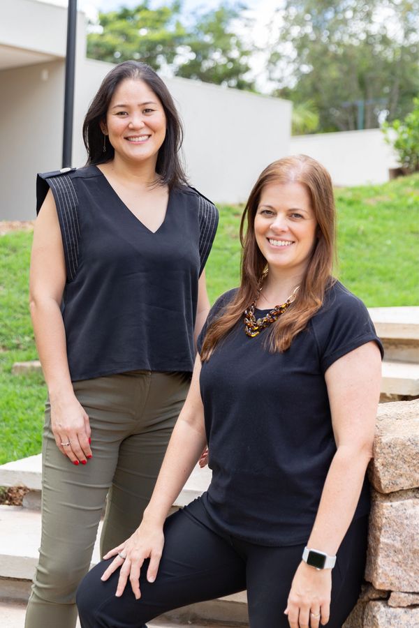 Two women smiling outdoors, dressed in black tops and casual pants.