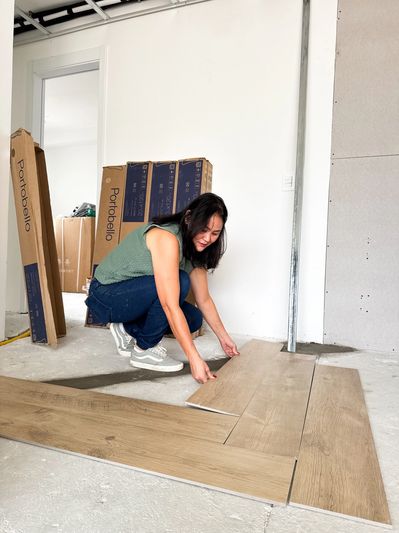Woman installing wooden flooring in a room under renovation.