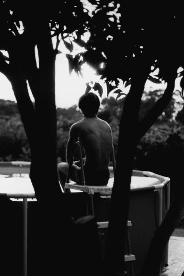 Homem sentado na borda de uma piscina ao ar livre.