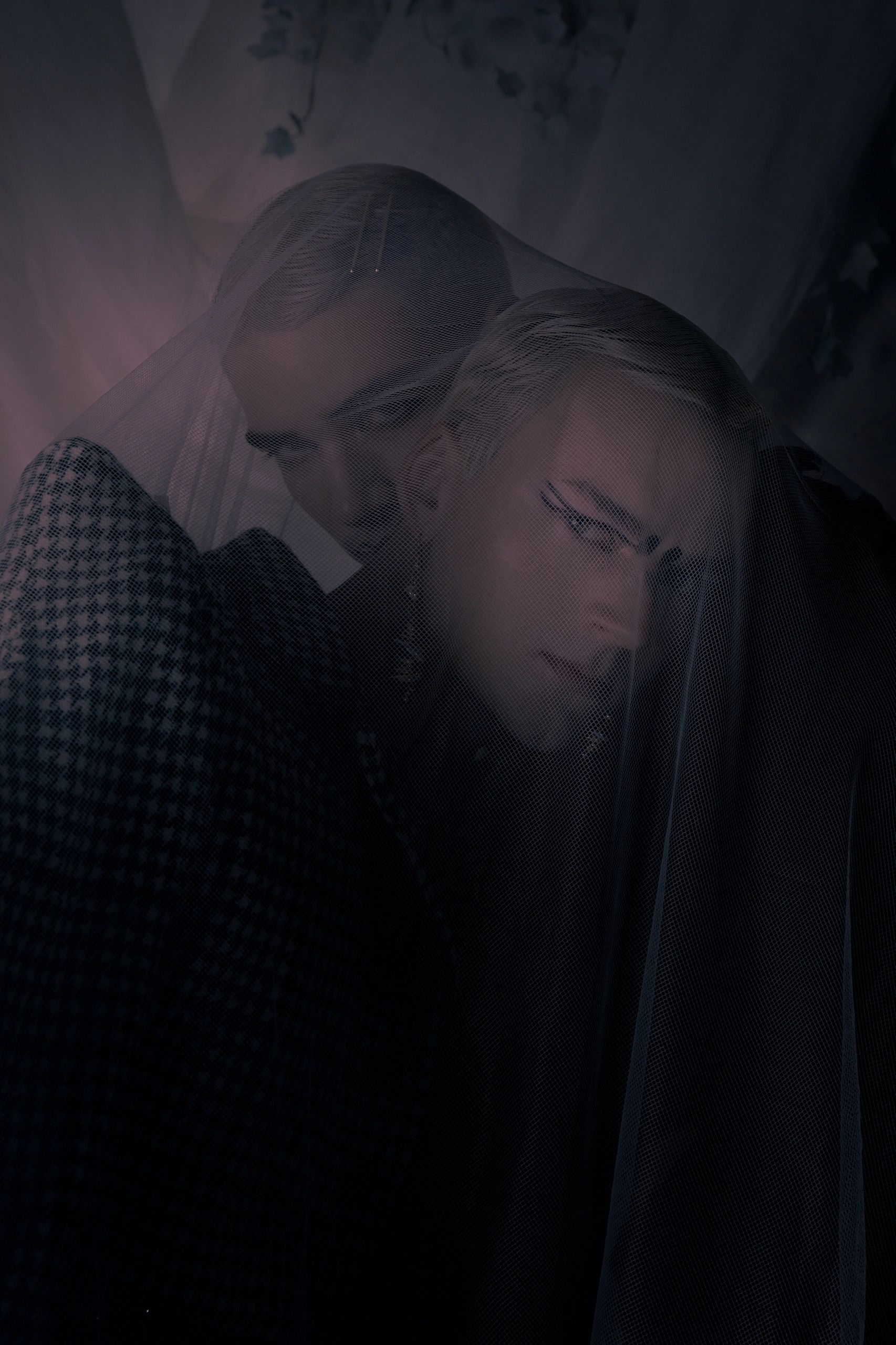 Two people under a sheer black veil in dim lighting.