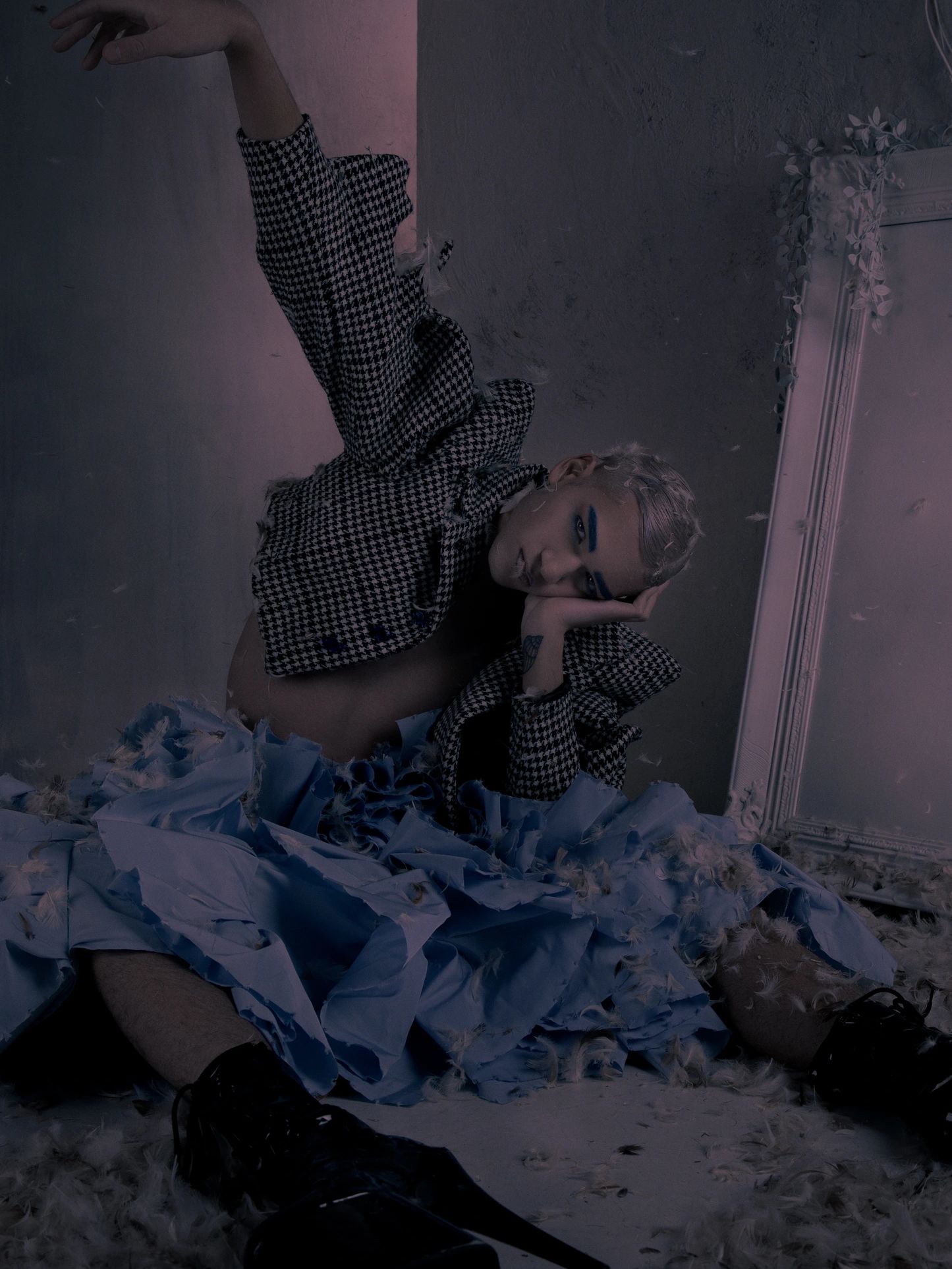 Person in dramatic pose amidst feathers and torn fabric.