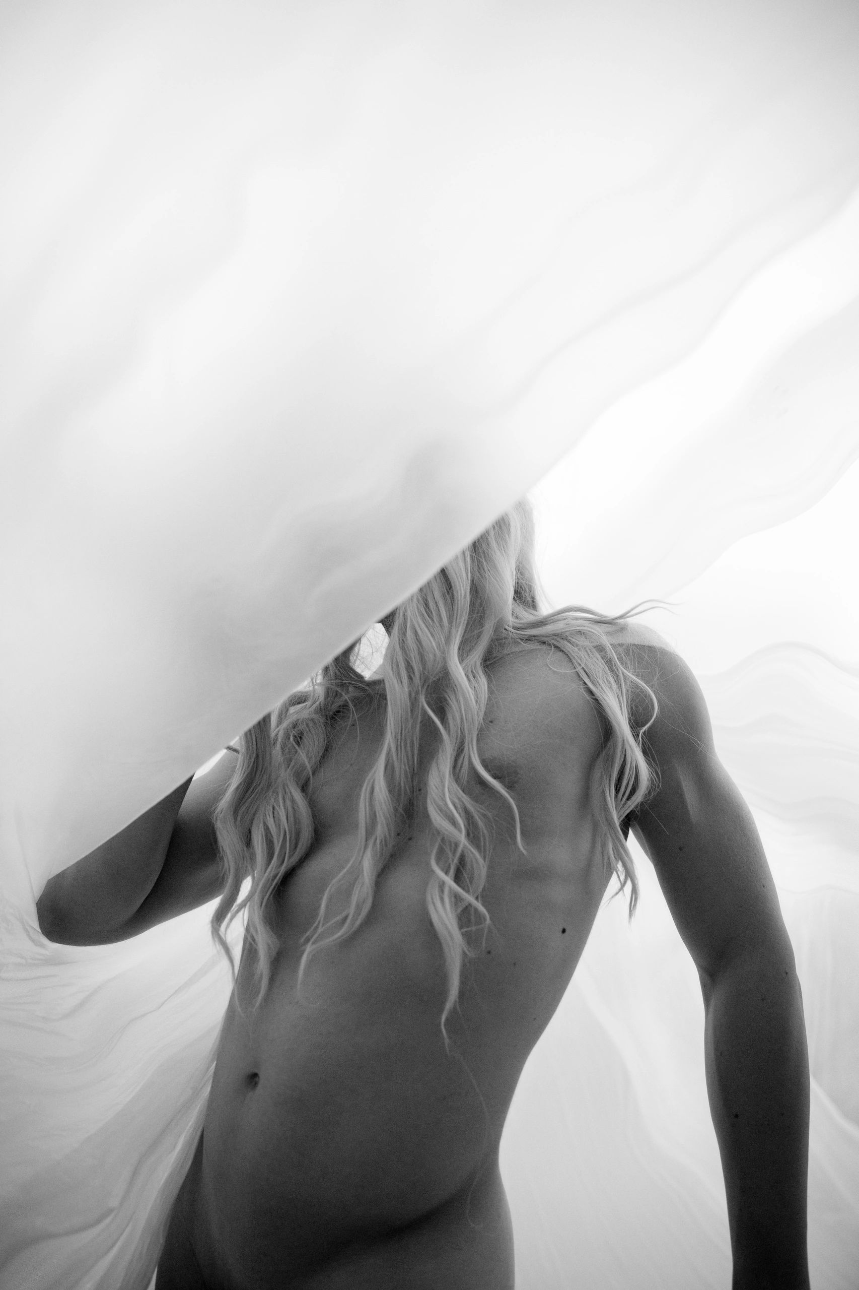 Black and white artistic photo of a woman behind flowing fabric.