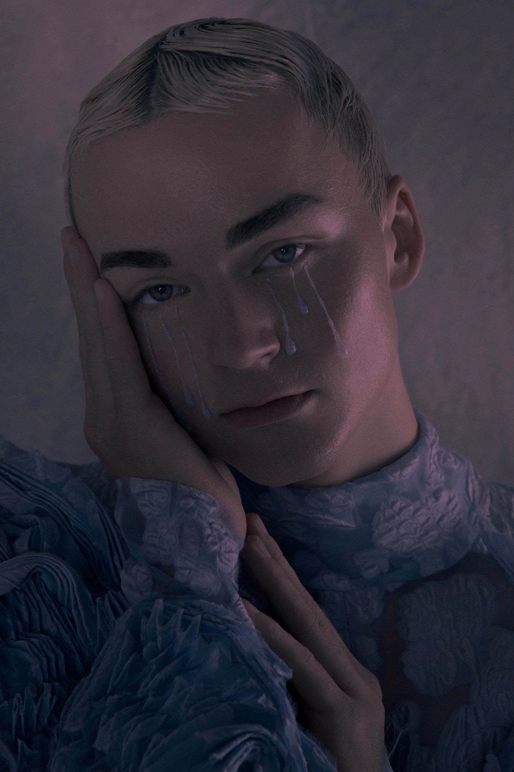 Person with artistic tear-like paint on face, touching their cheek.