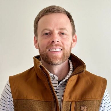 Smiling man in a brown vest against a plain background.