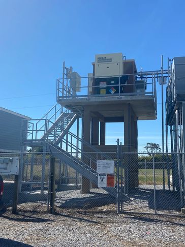 Elevated industrial control unit with stairs and safety fencing under clear blue sky.