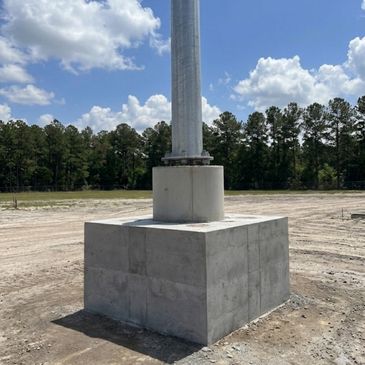 A tall metal pole mounted on a large concrete base outdoors.