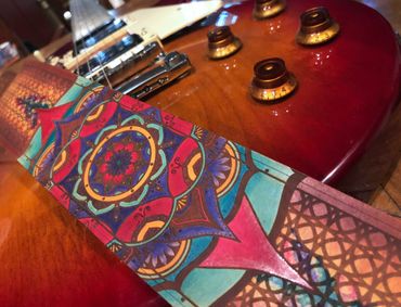 “Sunset mandala” on brown leather guitar strap, teal, red, gold and purple.  Flutterswine original 