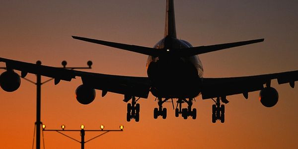 Rear view of a plane with landing gear down, silhouetted against a sunset sky with runway lights.
