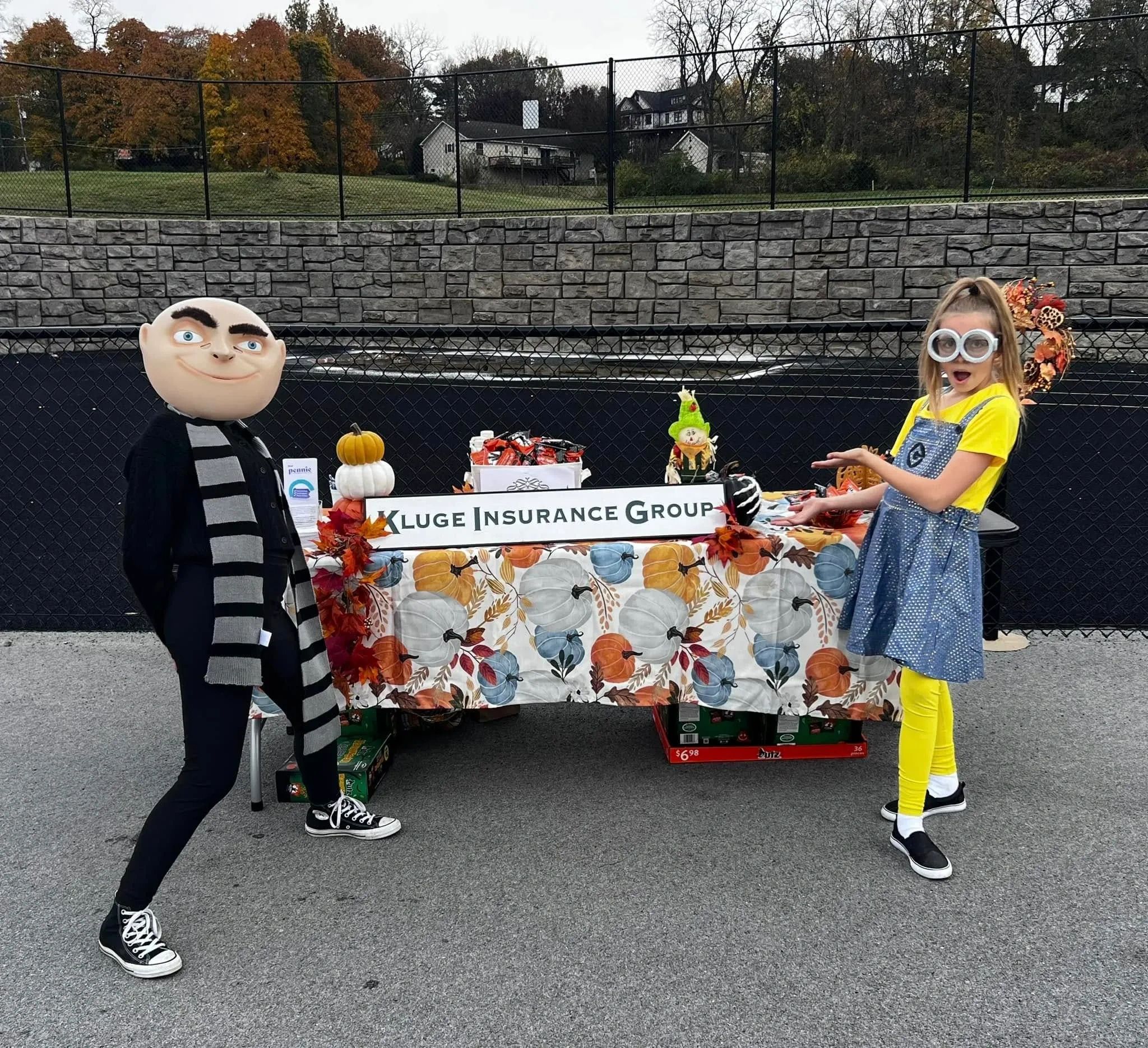 Two people in costumes posing at a festive insurance group booth outdoors.