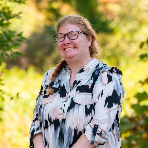 Smiling woman with glasses outdoors in a patterned blouse.