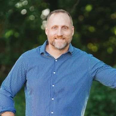 Smiling man in blue checkered shirt outdoors.