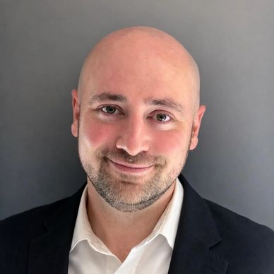 Smiling bald man in a black suit jacket and white shirt.