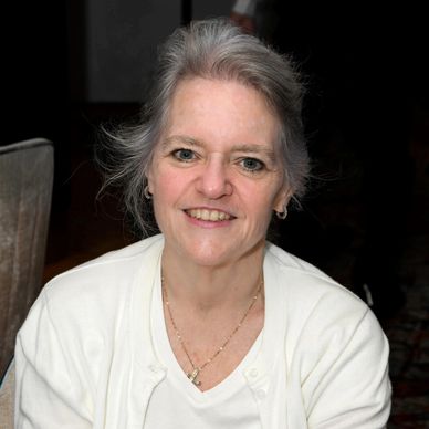 Smiling older woman with gray hair in white shirt.