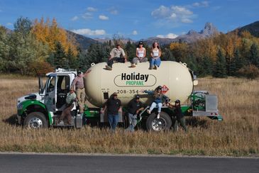 People posing on and around a propane truck in a field.