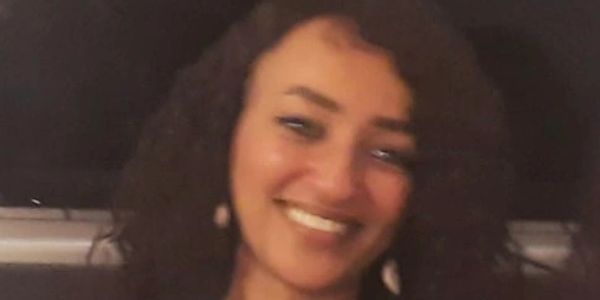Smiling woman with curly hair and earrings in a dimly lit setting.