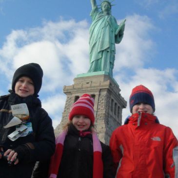 Three children in winter clothes in front of the Statue of Liberty.