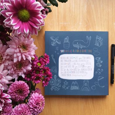 A book surrounded by pink and purple flowers on a wooden table.