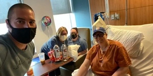 A group of four people in a hospital room, one in bed, all wearing masks.