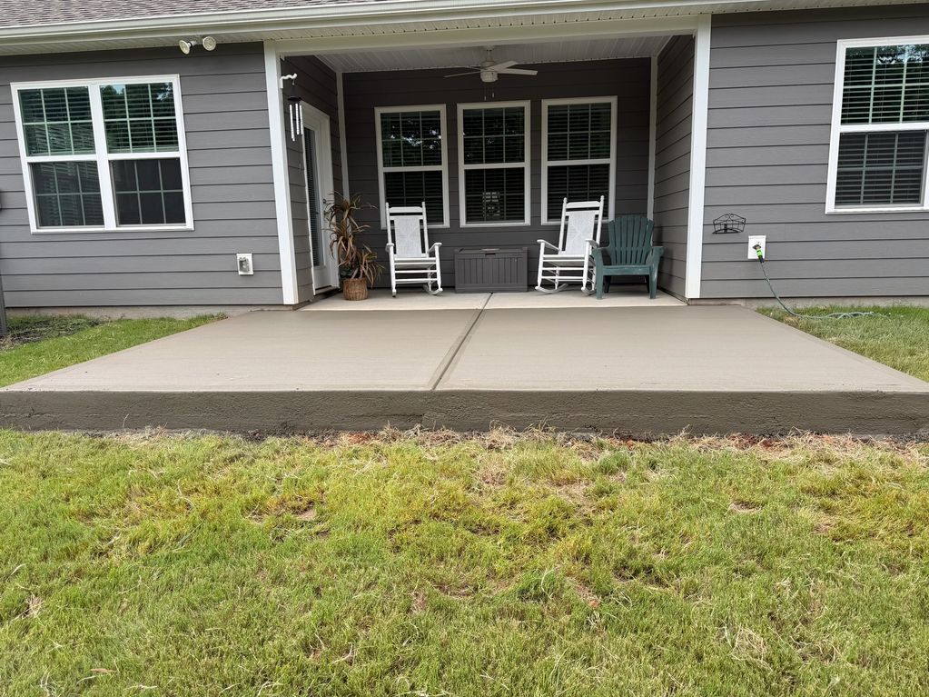 A newly poured concrete patio outside a house with chairs.