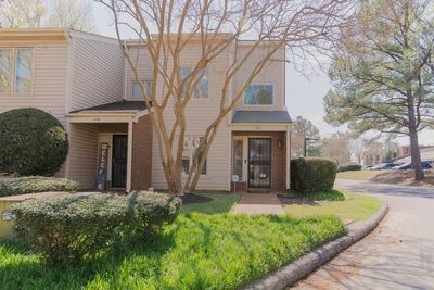 A townhouse with beige siding and a tree in the front yard on a sunny day.