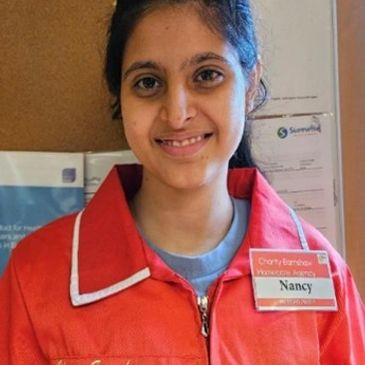 A woman named Nancy in a red charity uniform smiles at the camera.