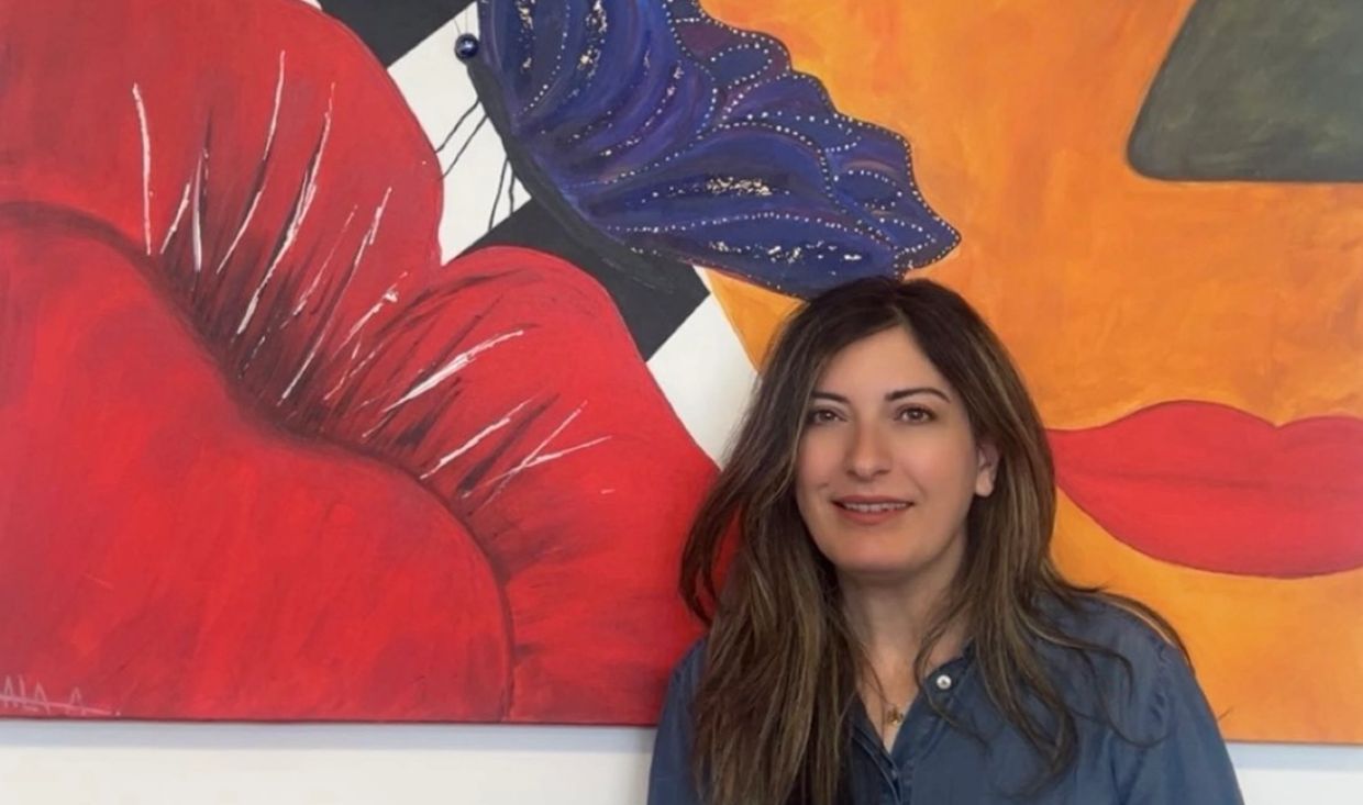 Woman smiling in front of colorful butterfly and flower mural.