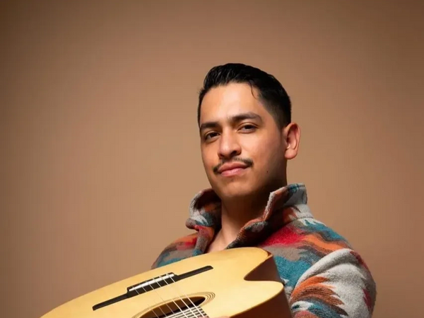 Man holding a guitar, smiling confidently.